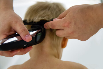 Kid boy with blond hairs getting his first haircut  with razor blade in a bathroom. Close up of...