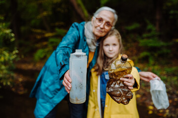 Small girl with grandmother showing plastic waste what they found outoors in forest.