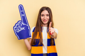 Young sports fan woman isolated on yellow background showing number one with finger.