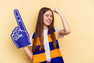 Young sports fan woman isolated on yellow background raising fist after a victory, winner concept.