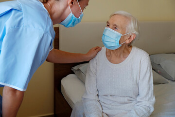 Mature female in elderly care facility gets help from hospital personnel nurse. Senior woman with...