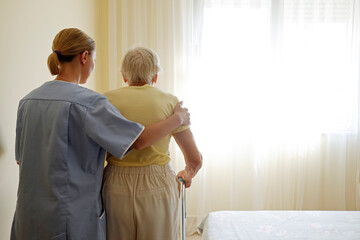 Senior woman holding quad cane handle in elderly care facility. Hospital nurse taking care of...