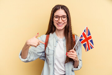 Young caucasian woman studying English isolated on yellow background person pointing by hand to a shirt copy space, proud and confident