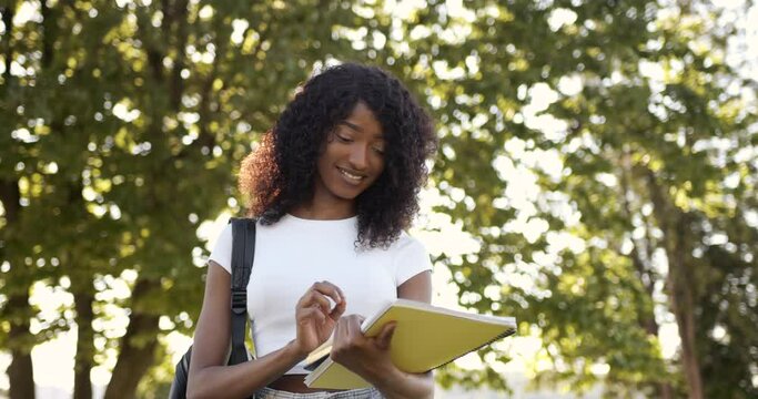 Smiling black woman student readng notebook in park