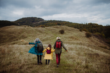 Rear view of small girl with mother and grandmother hiking outoors in autumn nature.