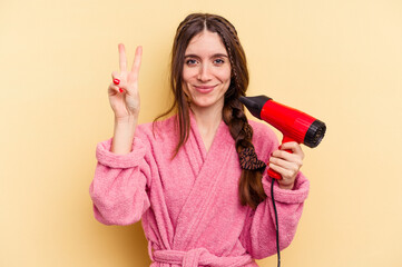 Young woman holding a hairdryer isolated on yellow background showing number two with fingers.