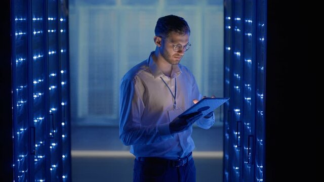 Male Server Engineer in Data Center. IT engineer inspecting a secure server cabinet using modern technology laptop coworking in data center.