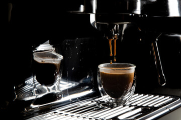 Dark coffee drops dripping in a transparent glass espresso cup on a manual espresso machine with copy space, close up