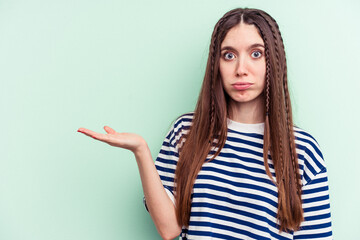 Young caucasian woman isolated on green background showing a copy space on a palm and holding another hand on waist.