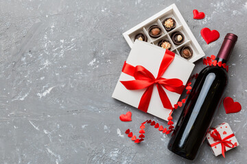 Bottle of red wine on colored background for Valentine Day with gift and chocolate. Heart shaped...