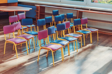Empty preschool classroom with multi colored chairs standing in rows