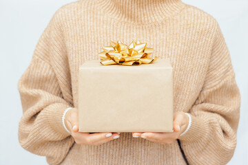 Woman's hands gift box with gold ribbon, woman in warm beige jumper Hold present box with bow. Mock...