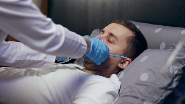 a doctor wearing personal protective equipment or PPE gives an oxygen mask to a European man with COVID-19 or coronavirus infection who has pneumonia in a hospital isolation ward. medical concept
