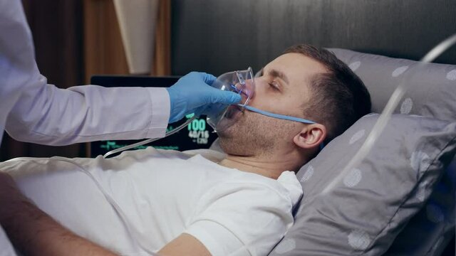 a doctor wearing personal protective equipment or PPE gives an oxygen mask to a European man with COVID-19 or coronavirus infection who has pneumonia in a hospital isolation ward. medical concept