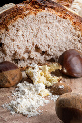 A loaf of bread made with chestnut flour with whole chestnuts on a wooden chopping board.