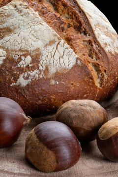 A loaf of bread made with chestnut flour with whole chestnuts on a wooden chopping board.