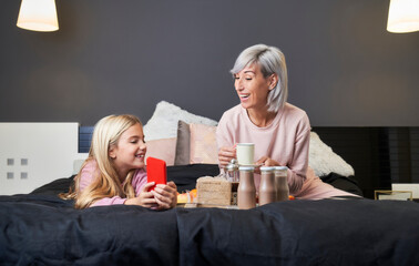 mother and daughter in pajamas having breakfast in bed. happy family moments portrait