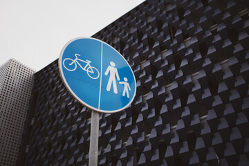 Round blue signposted with pictograph of pedestrians and bicycle in front of a modern building...