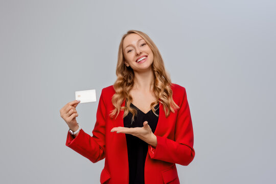 Image of smiling good-looking businesswoman showing credit card, demonstrating bank product, shopping website, standing against gray background