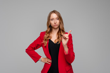 Serious female entrepreneur with fair hair in red and black clothes pointing finger up, scolding or...