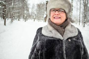 An elderly woman walks in a winter city park.