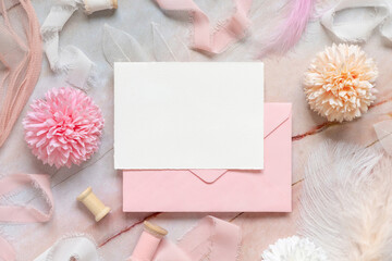 Card and pink envelope near pastel flowers, silk ribbons and feathers on marble