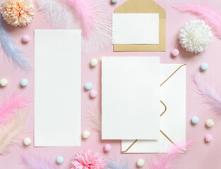 Blank cards and envelope near pastel flowers, pom-poms and feathers near ring in a gift box on pink