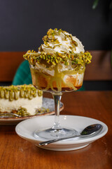 Caffè freddo al pistacchio con panna montata e granella di pistacchio servito su un tavolo di legno e con una cheesecake al pistacchio sullo sfondo