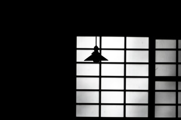 暗い部屋の格子の影の前に映る、天井からつり下がるランプ照明の影