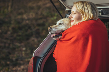 A beautiful woman hugs her Golden Retriever dog and covers her with a red blanket from the cold....