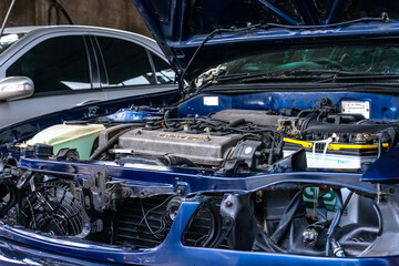 under repair blue car with many unmounted parts on the engine bay with the hood opened at the auto...