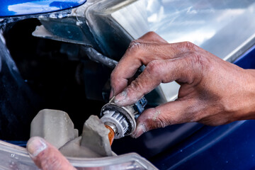 Man mechanic installing the turn light bulb with his hands into the headlamp house of blue car at...