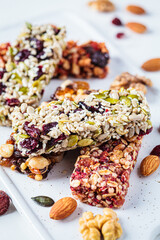 Energy granola bars with different seeds, nuts and dried fruits and berries on white marble background. Healthy snack concept.