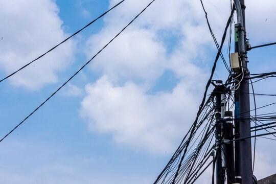 electric and telecommunication poles with messy cables stand under the bright blue sky