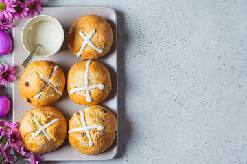 Traditional Easter cross buns with raisins on a background with flowers and colored eggs.