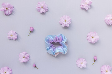 One shiny scrunchie and fresh spring cherry blossom pink flowers on pastel backround. Flat lay, top view. Diy accessories, hairstyle, lifestyle, spring outfit ideas concept, copy space