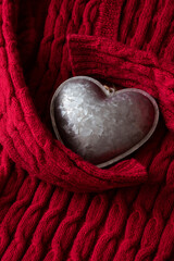 Silver metal textured heart embraced by red cable knitted sweater