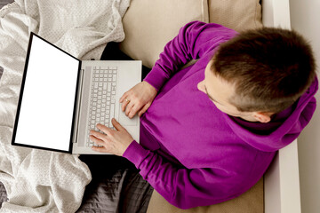 Fototapeta na wymiar Man relaxing on bed and holding laptop computer. Mock up with blank white screen. Man using notebook to surf in internet, read news, watch movie, study or work online. App, game, web site presentation