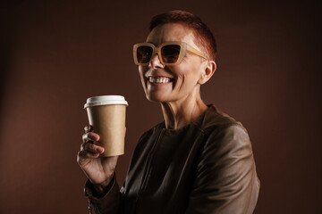 Senior ginger woman in sunglasses drinking coffee takeaway