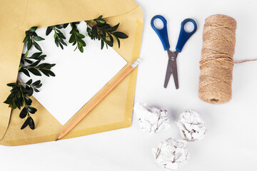 Craft paper envelope with empty paper and green twigs among crumpled paper and bundle winding on white background