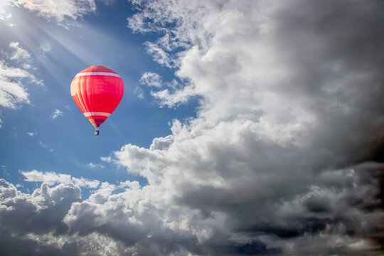 a red hot air balloon soaring into clouds of a summer storm