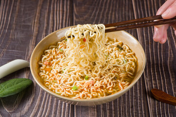 chopsticks with cooked instant noodles on wooden background