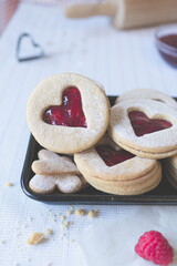 Portrait angled shot of three heart shape linzer cookies and raspberry jam on a white background. Valentines day, love and romance food concept image.