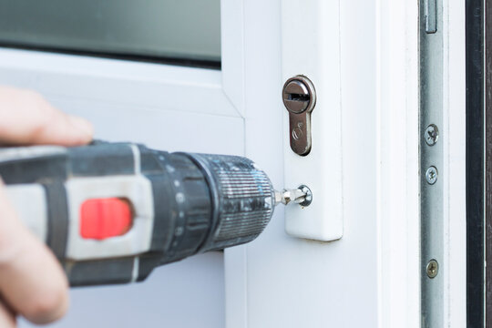 Handyman check door lock with screw gun in front plastic door. Checking lock close up for operability in door.