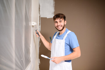 handsome young man professional painter in construction site wall painting renovation in a client house - obrazy, fototapety, plakaty
