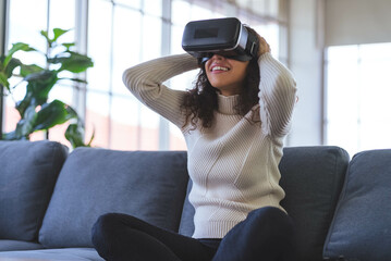 Young African American woman wearing virtual reality glasses is playing vr video games on sofa at home. Stay at home and self-quarantine in spread of coronavirus covid-19