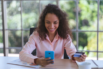 Young latin woman smiling and using smartphone for online shopping. Business woman and freelance work from home and holding credit card for electronic payment. happy shopper services in online store.