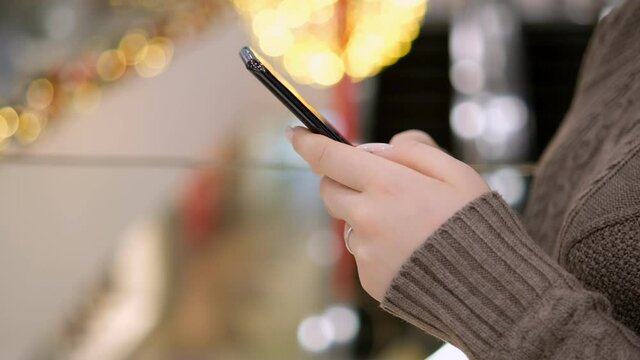 Business woman in shopping mall. Young female hands touch the phone. Woman in a sweater with a with a smartphone. Tapping, scrolling, watching video, content, bloggs. Modern lifestyle. Young woman in