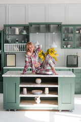 Beautiful modern woman in the kitchen at home. Plaid pajamas. Yellow flowers in the interior. Table, dishes, design.