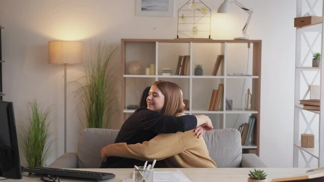 Family reconciliation. Problem solution. Parents agreement. Gloomy mother and teenage daughter embracing after quarrel sitting desk light home interior.